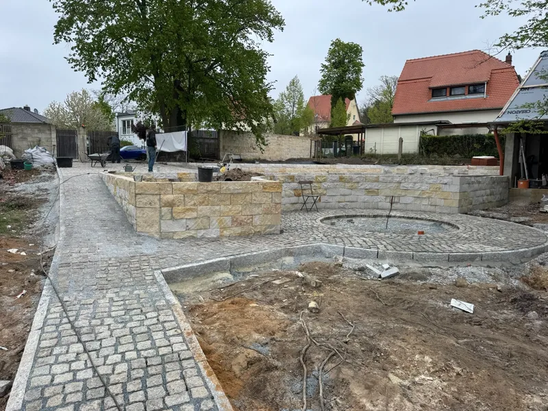 Gepflasterter Gartenbereich mit kreisförmiger Fläche und Natursteinmauern