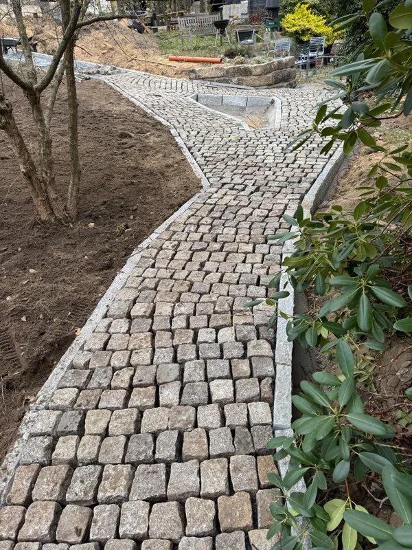 Geschwungener Pflasterweg mit Granitborden zwischen Gartenflächen